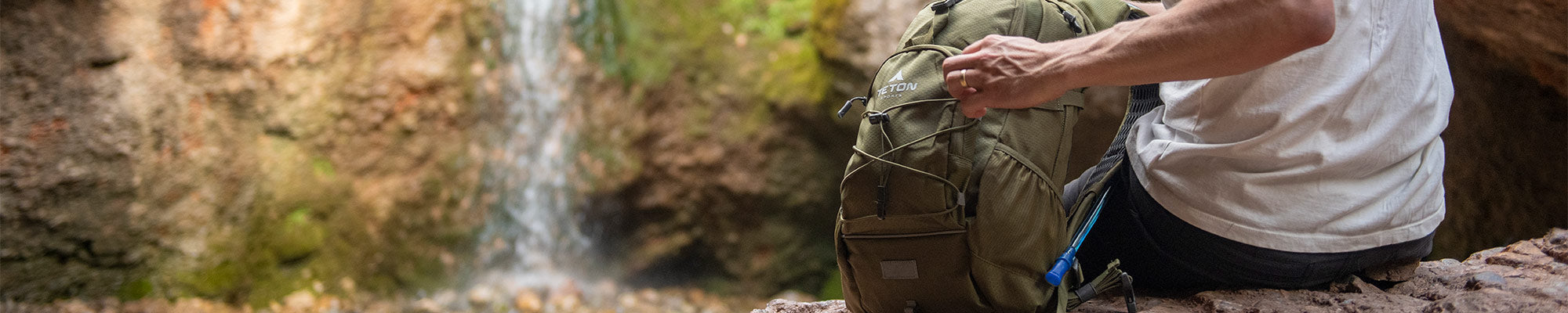 A man opens his TETON Sports Oasis Backpack with a waterfall in the background.