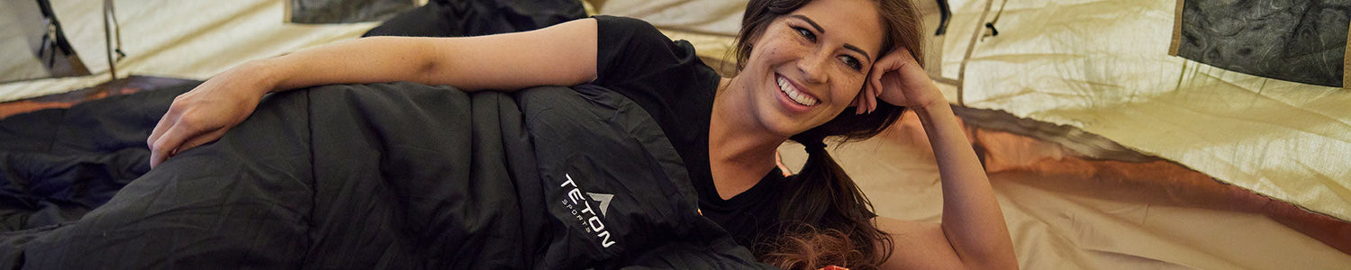 A woman lays in her Evergreen TETON Sports sleeping bag inside a canvas tent.
