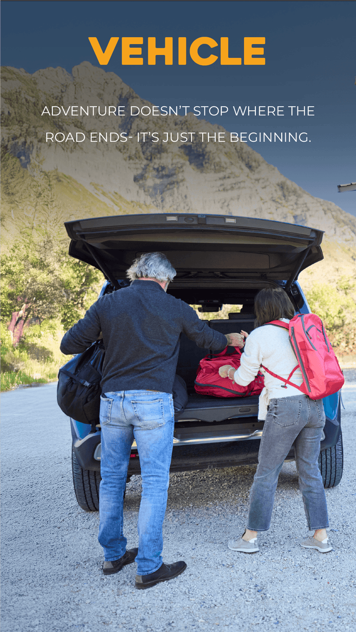 VEHICLE SOLUTIONS Two people loading a suitcase into an open car trunk with a scenic mountain background.