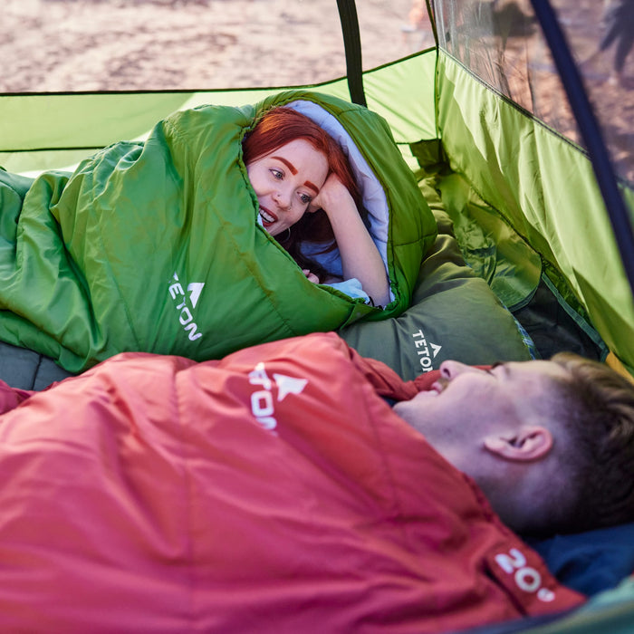 Two people lying in leef mummy sleeping bags inside a tent, with visible branding.