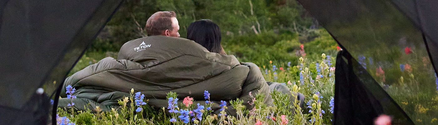 A man sits inside his TETON Sports Celsius XXL Sleeping Bag while viewing a valley below.