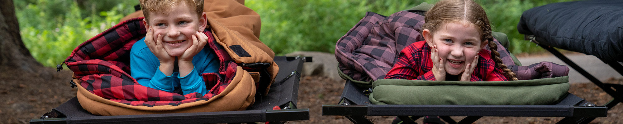 Two children smile for the camera while snuggled into their TETON Sports L'il Bridger Canvas Sleeping Bags.