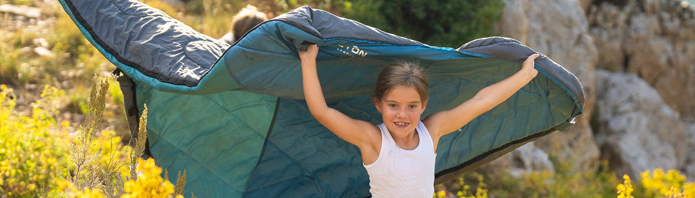 A child runs through a field of wildflowers holding a TETON Sports Celsius Sleeping Bag.