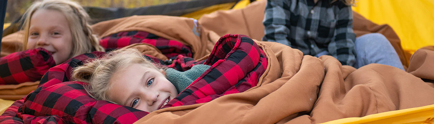 Three children snuggle together in a TETON Sports Vista Tent using their Deer Hunter Canvas Sleeping Bags.