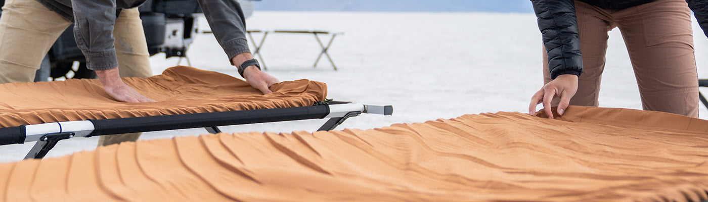 A couple rolls out their TETON Sports canvas camp pads onto their TETON Sports camp cots.