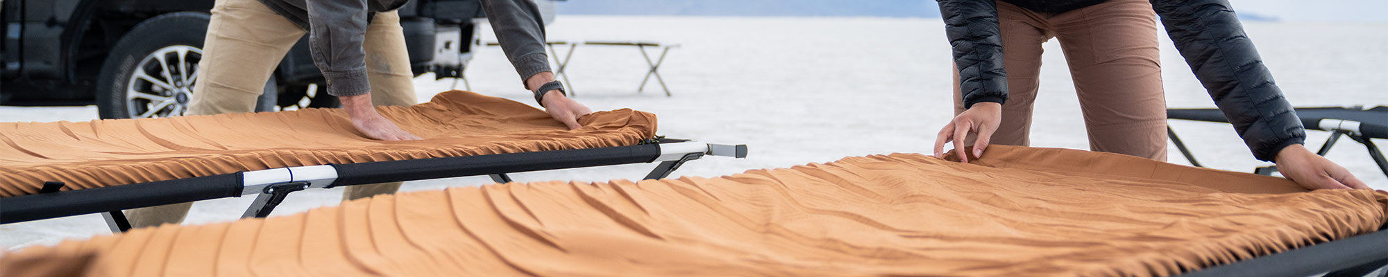 A couple rolls out their TETON Sports canvas camp pads onto their TETON Sports camp cots.