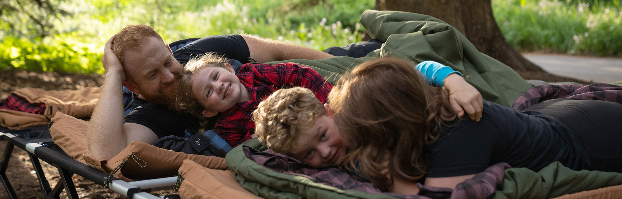 New Bridger Canvas Sleeping Bags: Image shows a family of four snuggled up in TETON Sports Bridger Canvas Sleeping Bags. There are two adults and two children and they are lying on TETON cots and sleeping pads.