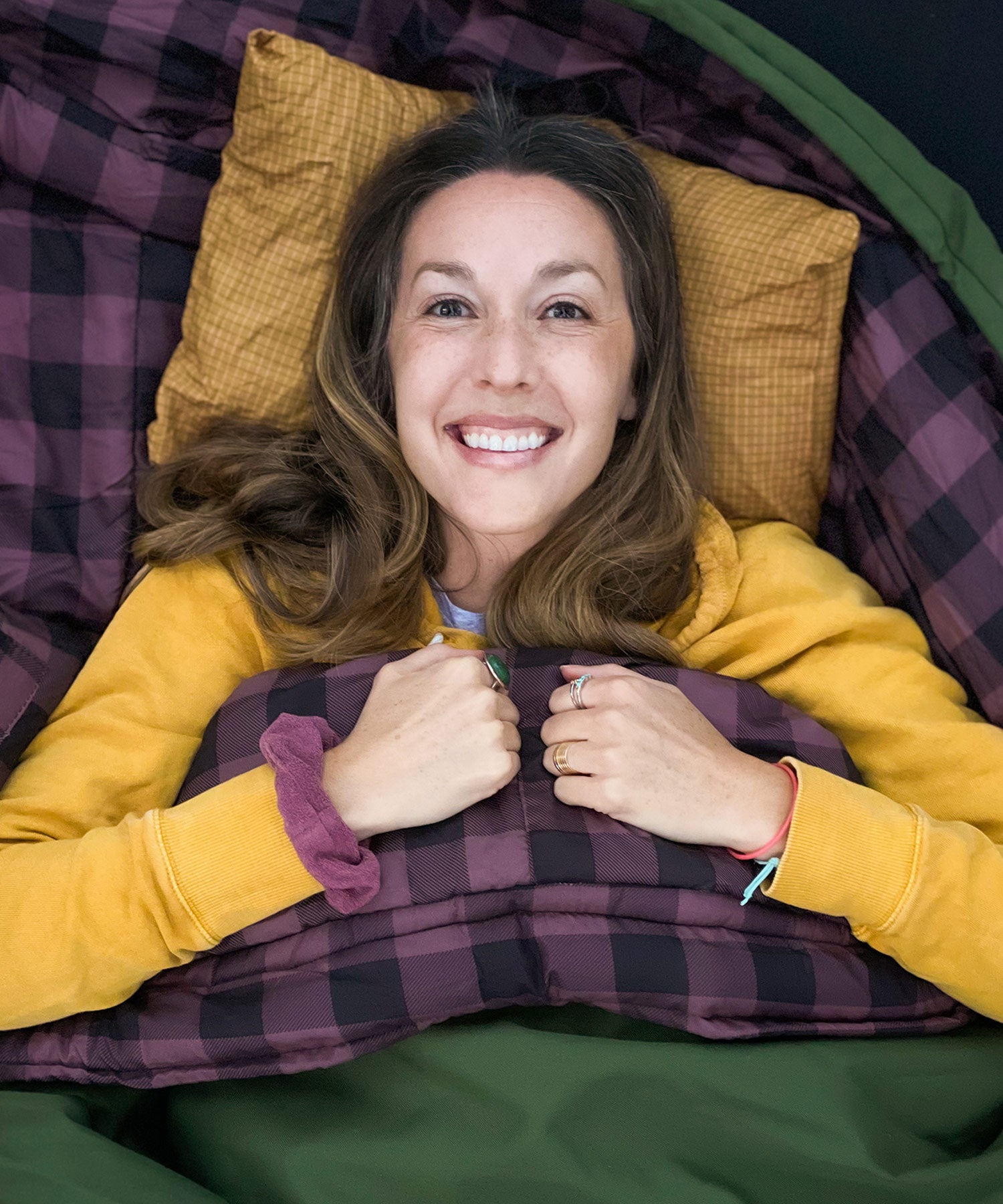 Image shows a woman smiling while snuggled in a green TETON Sports Bridger Canvas Sleeping Bag.