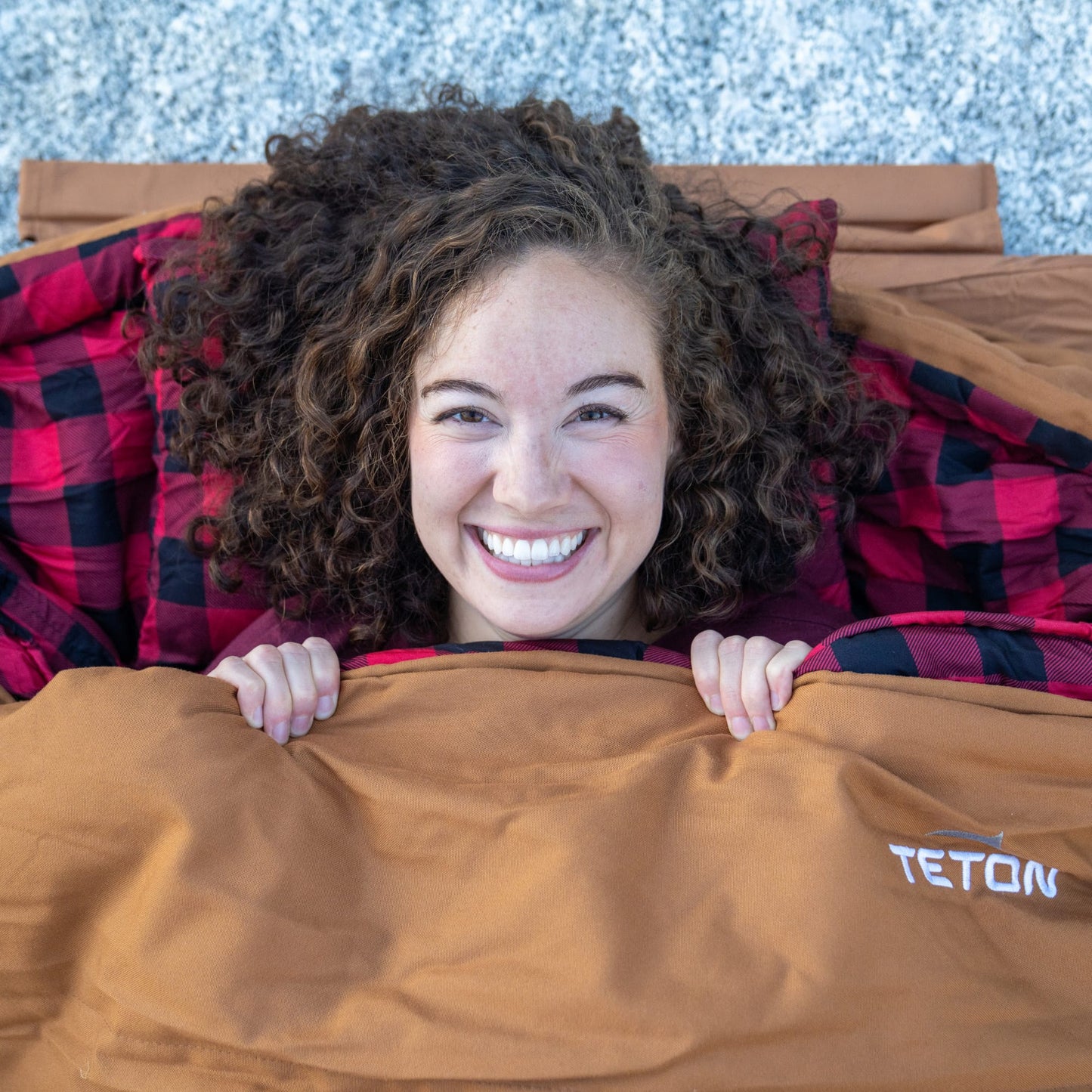 Person peeking out from under a bridger sleeping bag with TETON branding.