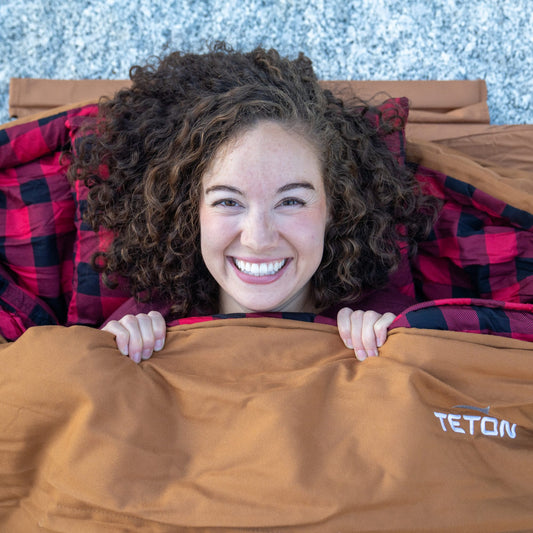 Person peeking out from under a bridger sleeping bag with TETON branding.