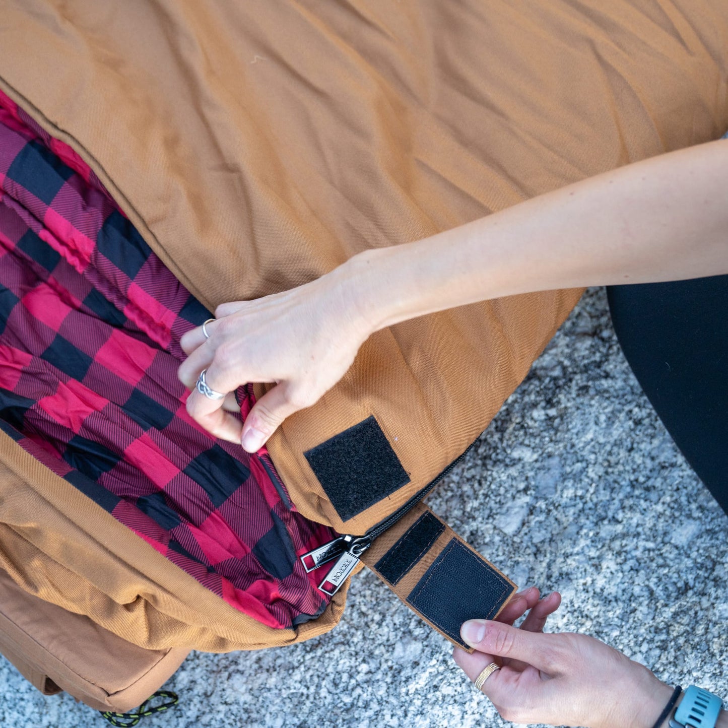 Person opening a bridger sleeping bag with red and black plaid lining.