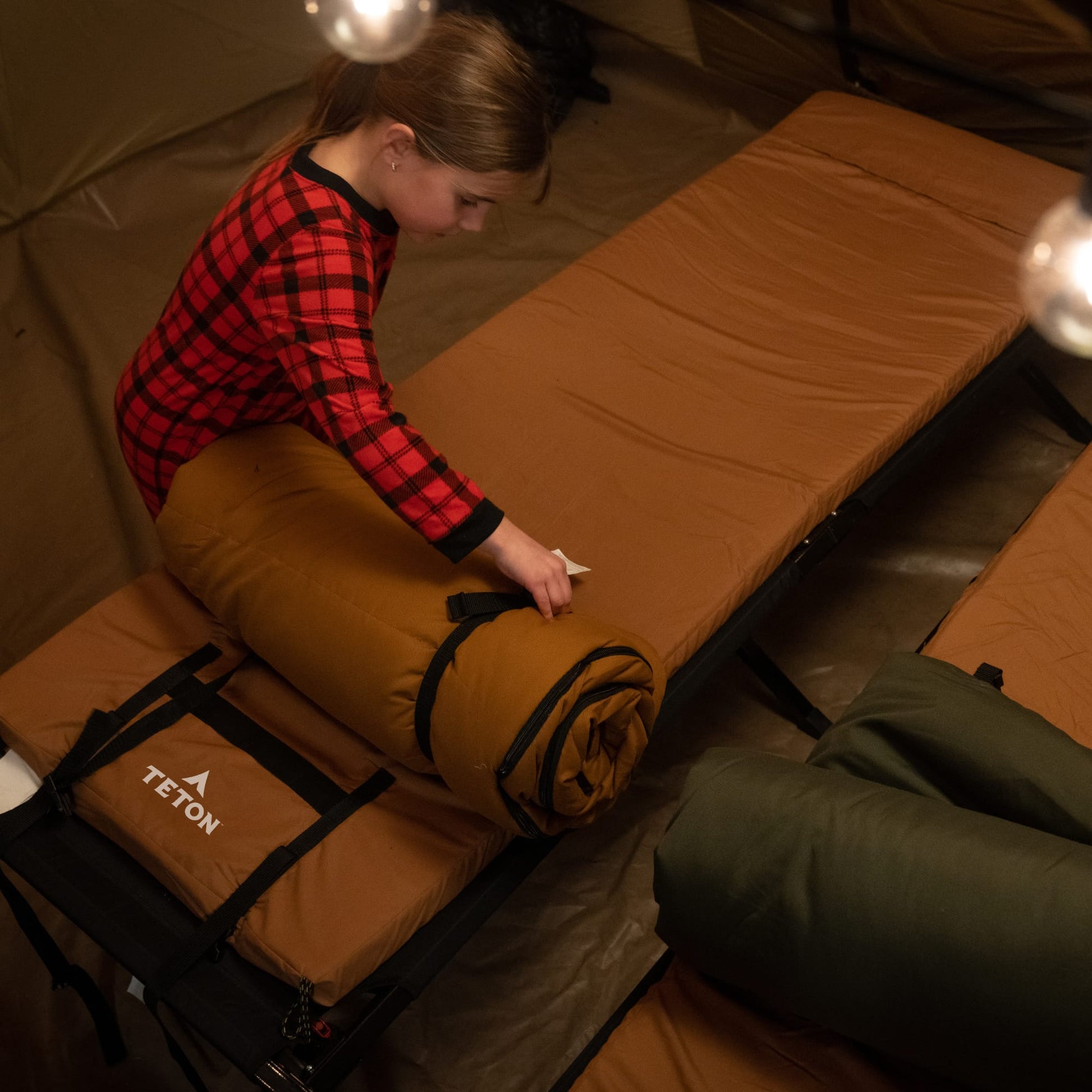 A kid setting up Bridger sleeping bag on a bed inside a tent