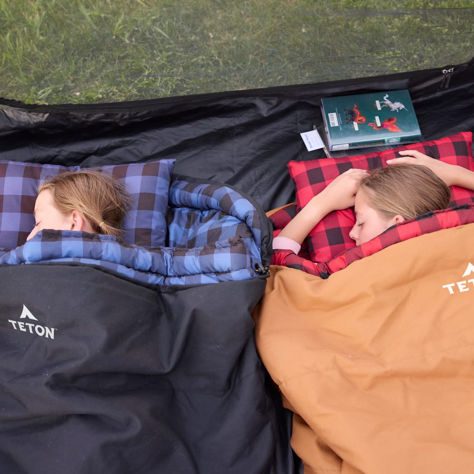 Two people lying in bridger sleeping bags with Teton brand labels, one reading a book.