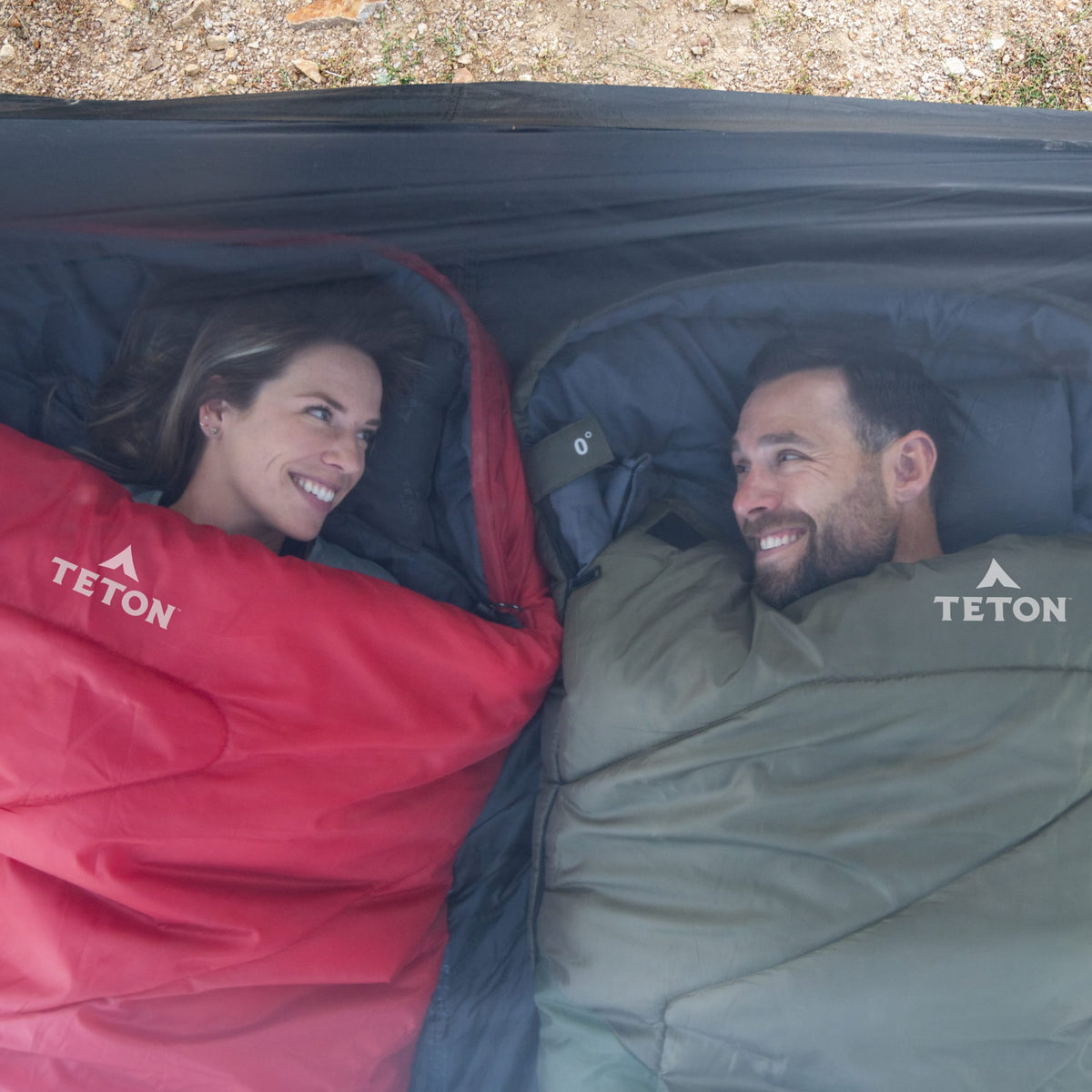 Two people lying in Teton Celsius sleeping bags, smiling at each other.