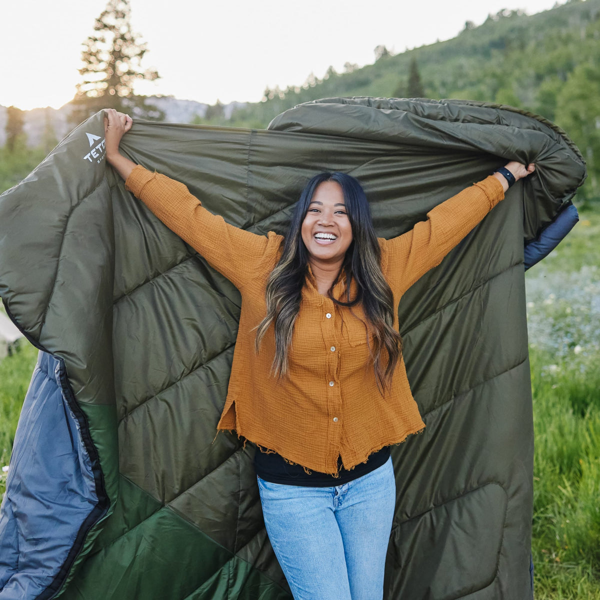 Person holding a mammoth celsius ivy sleeping bag outdoors with a scenic background