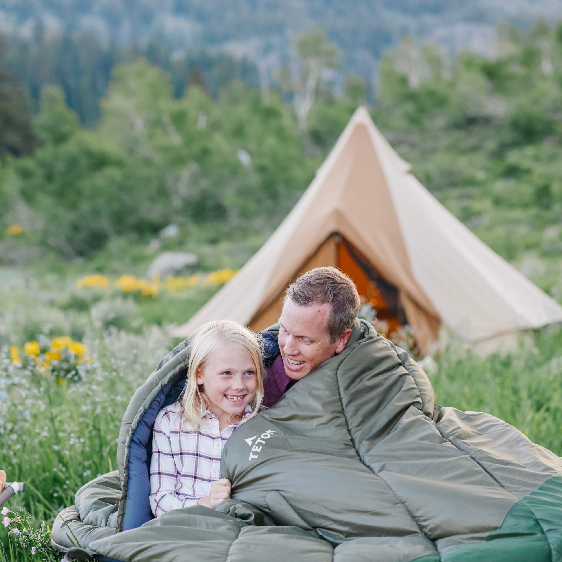 Father and Daughter lying in the Ivy Celsius sleeping bags with a tent in the background