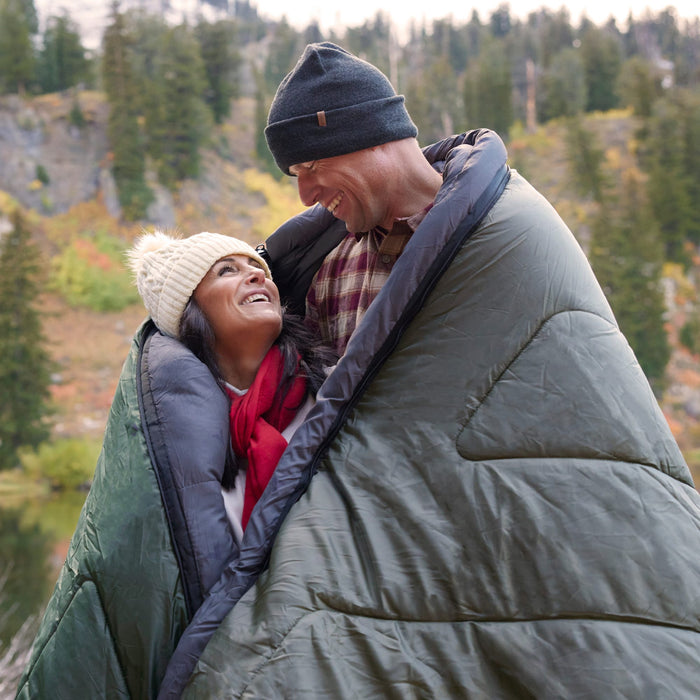 Two people hugging in a Mammoth Celsius Ivy sleeping bag with a forest in the background
