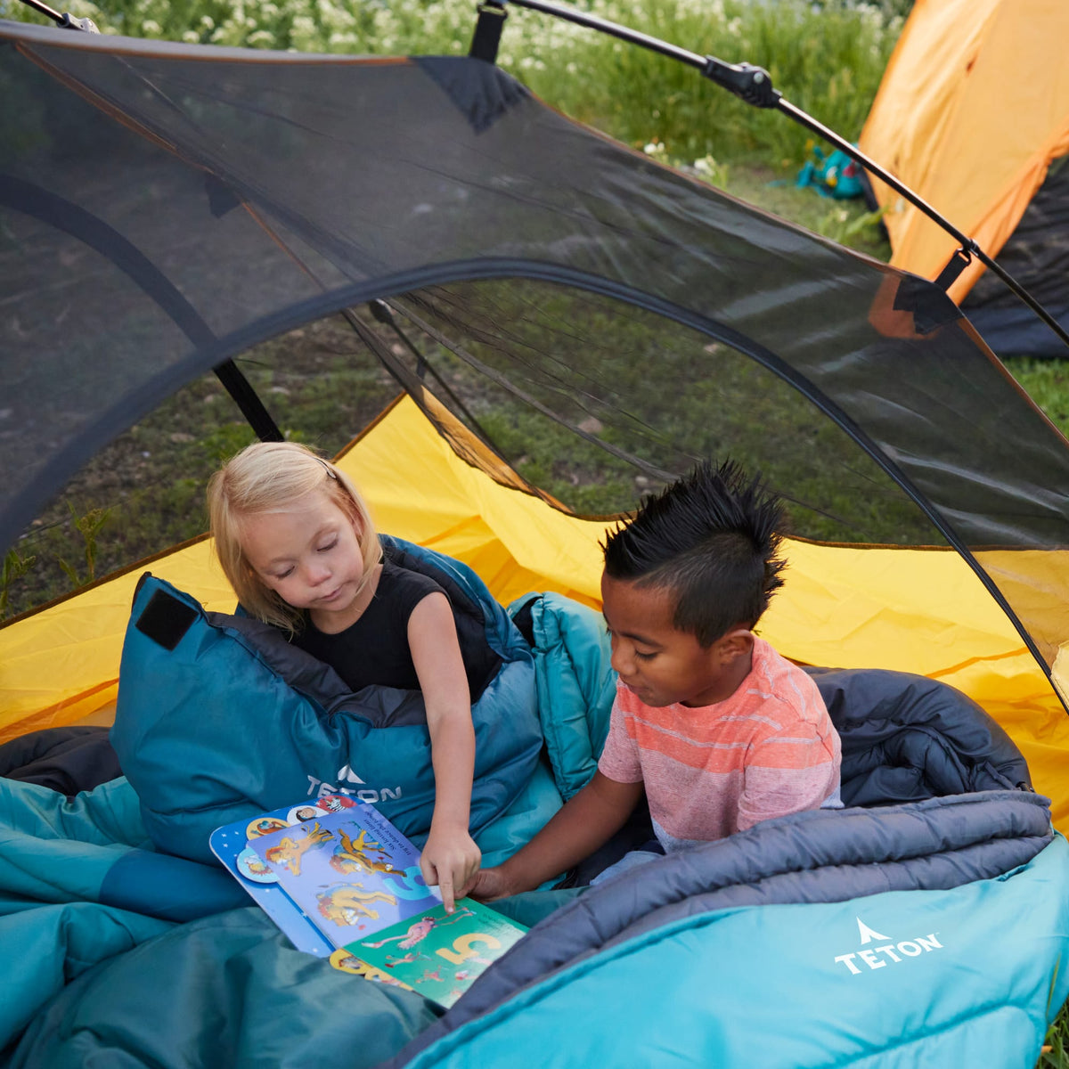 Two children reading a book inside a camping tent wrapped in ocean celsius jr  with Teton brand