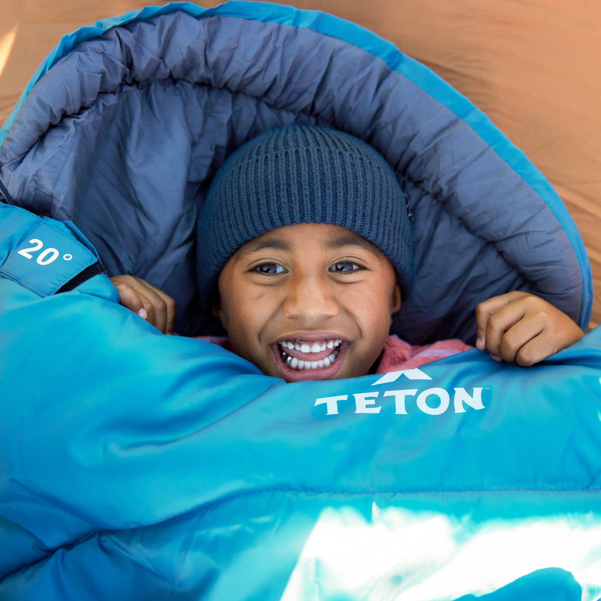 Child peeking out of a  ocean celsius jr  sleeping bag labeled 'Teton' 