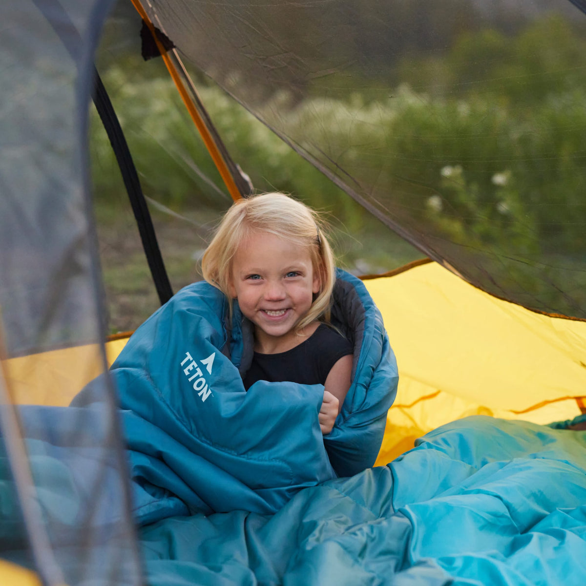 Child wrapped in a ocean celsius jr Teton sleeping bag inside a tent with a forest background