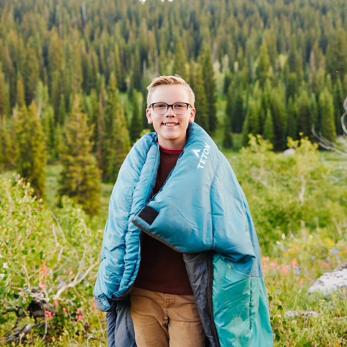 a child wrapped in a ocean celsius jr  sleeping bag with a forest in the background