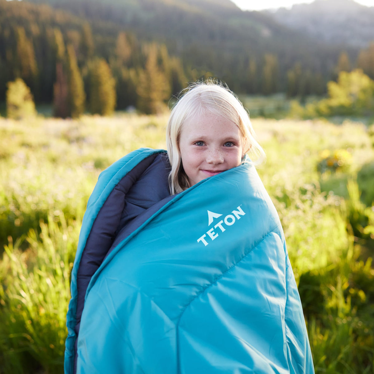 A kid wrapped in a ocean celsius jr sleeping bag in a forest setting