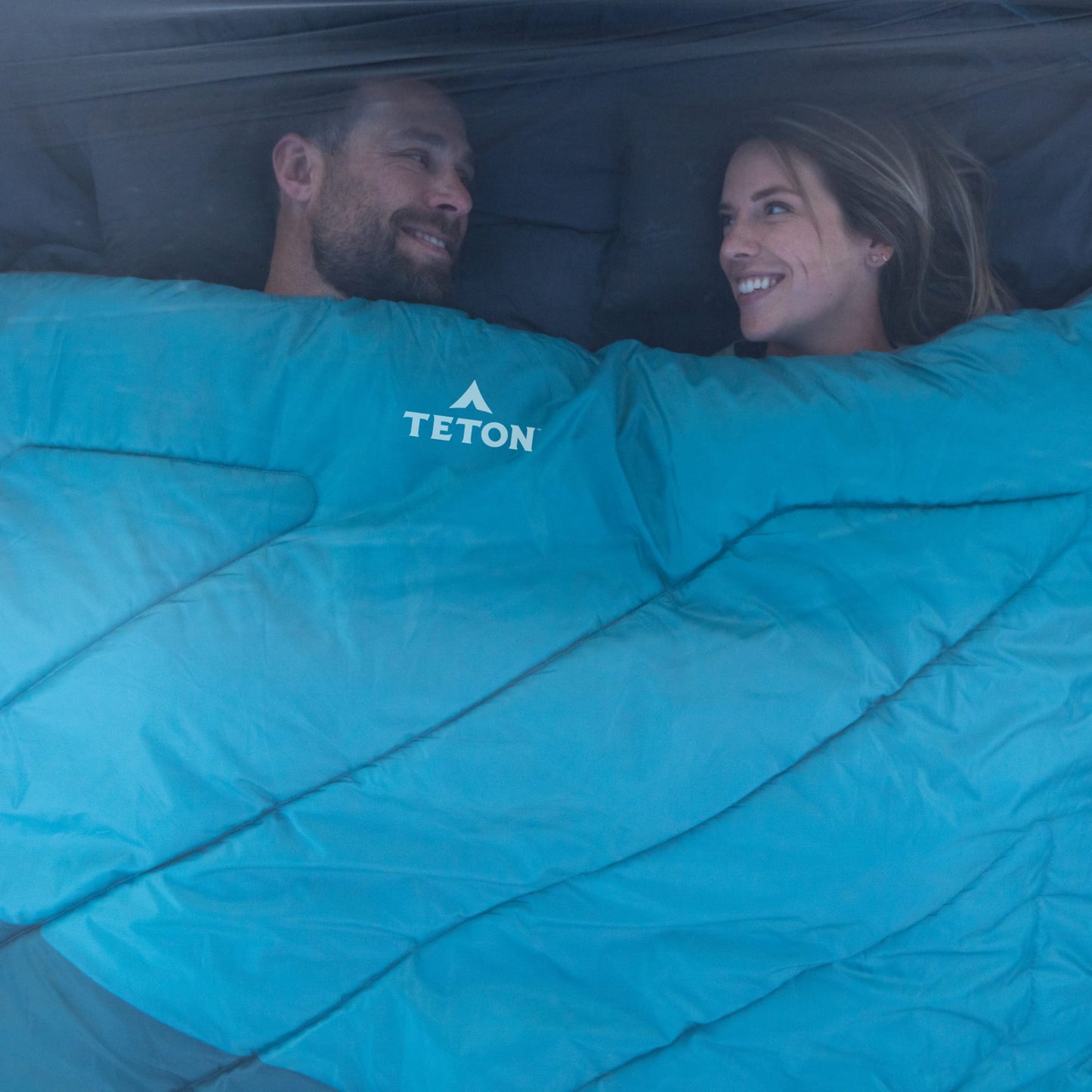 Two people lying in a mammoth celsius sleeping bag with Teton brand logo.