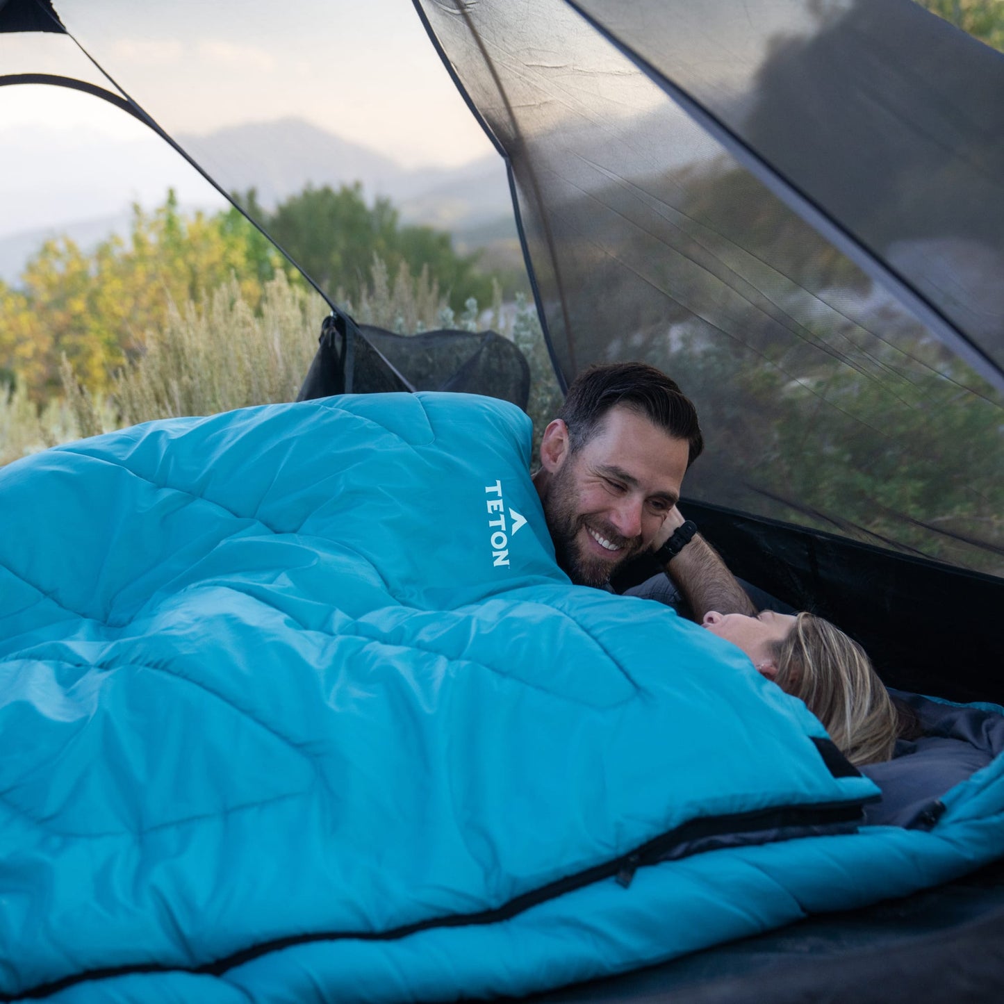 Two people lying in a mammoth celsius sleeping bag with Teton brand logo.