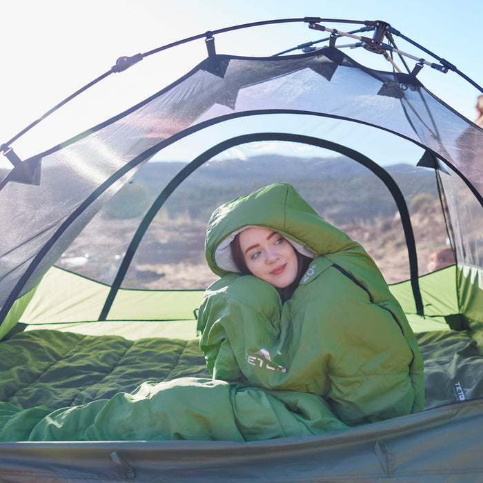 Person wearing a leef mummy sleeping bag in a tent with a scenic background