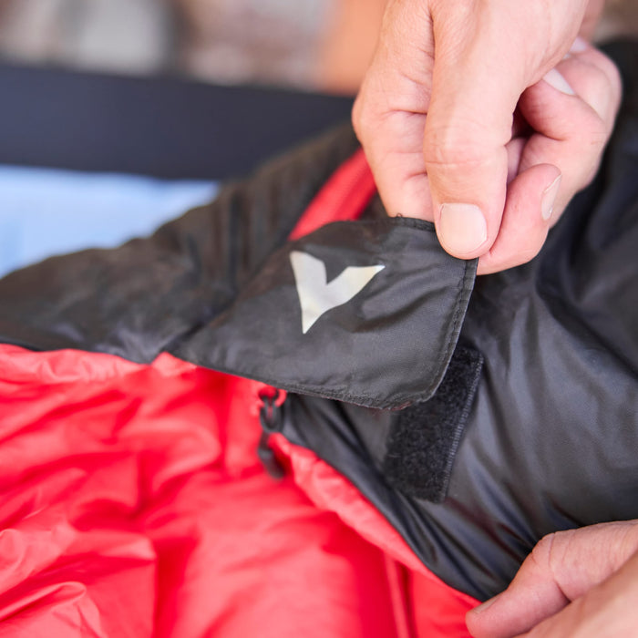 Person adjusting a red sleeping bag with a brand logo on a blurred background