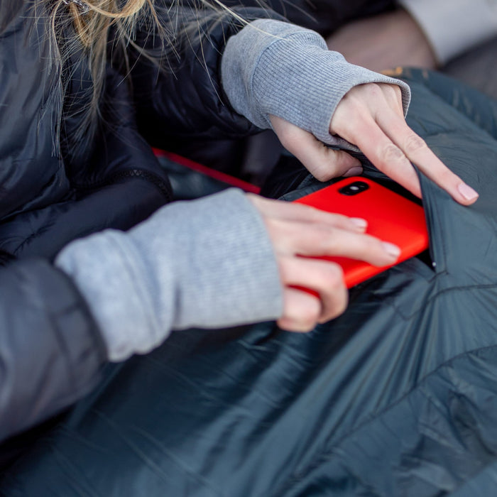 Person in a dark jacket with gray sleeves inserting a red phone, on altos mummy sleeping bag pocket