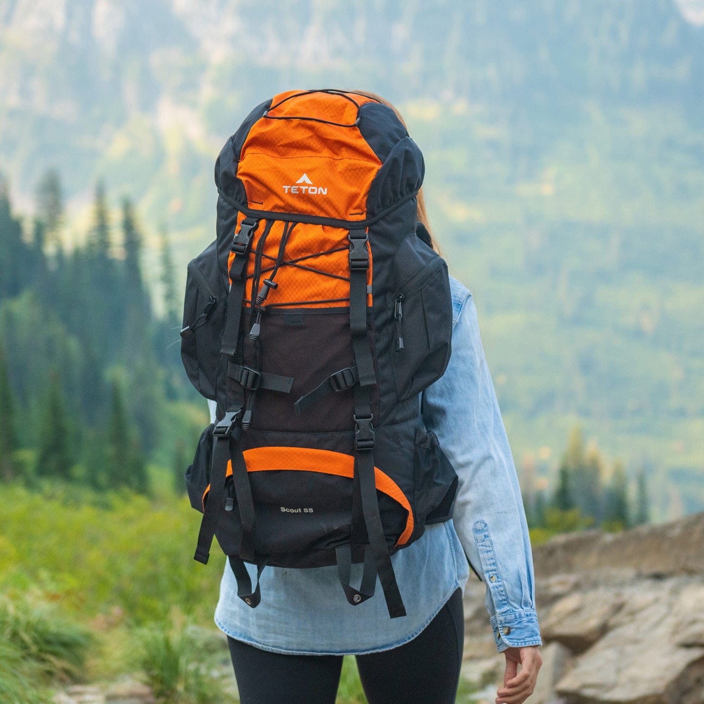 Person wearing a 55L orange and black backpack with a mountainous landscape in the background