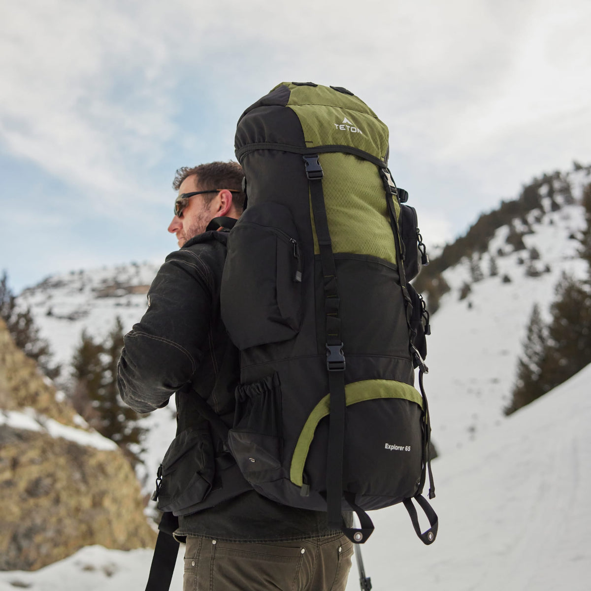 Person hiking in a snowy mountain landscape with a large 65L green and black backpack.