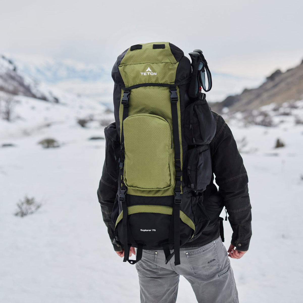 Person wearing a 75L green and black backpack with Teton brand in a snowy landscape