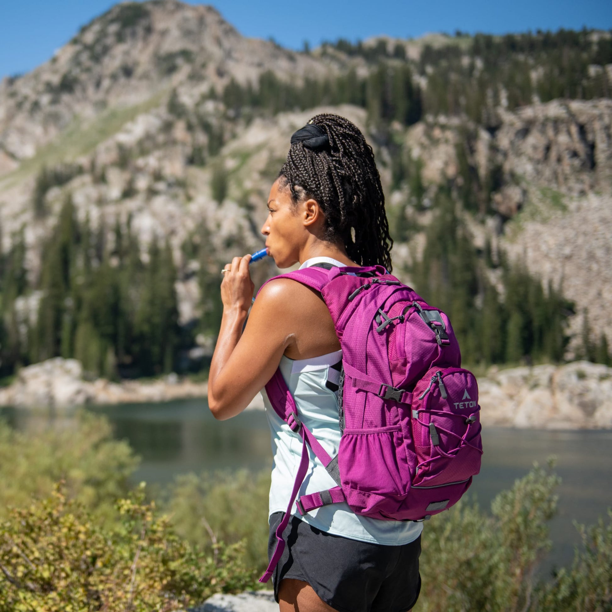 Person with a purple hydration backpack standing in a mountainous area with a lake.