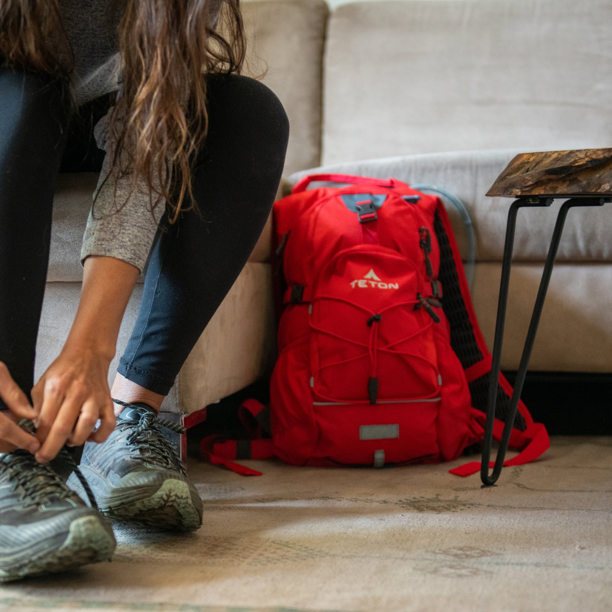 Person preparing to travel with red hydration backpack on a couch.