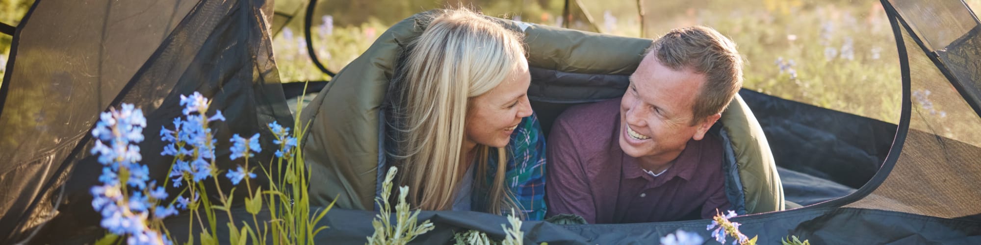 2 People in a sleeping bag inside a tent smiling.