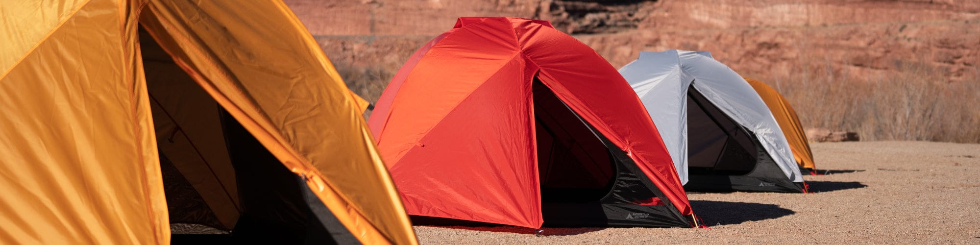 Three colorful mountain ultra tents set up outdoors on a sandy surface in a canyon place.