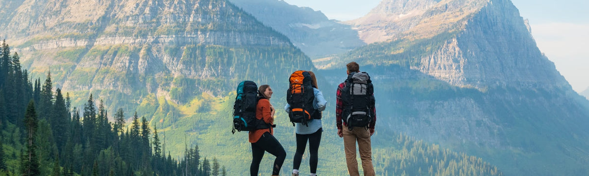 Three hikers wearing backpacking packs pausing to take in a mountain valley view.
