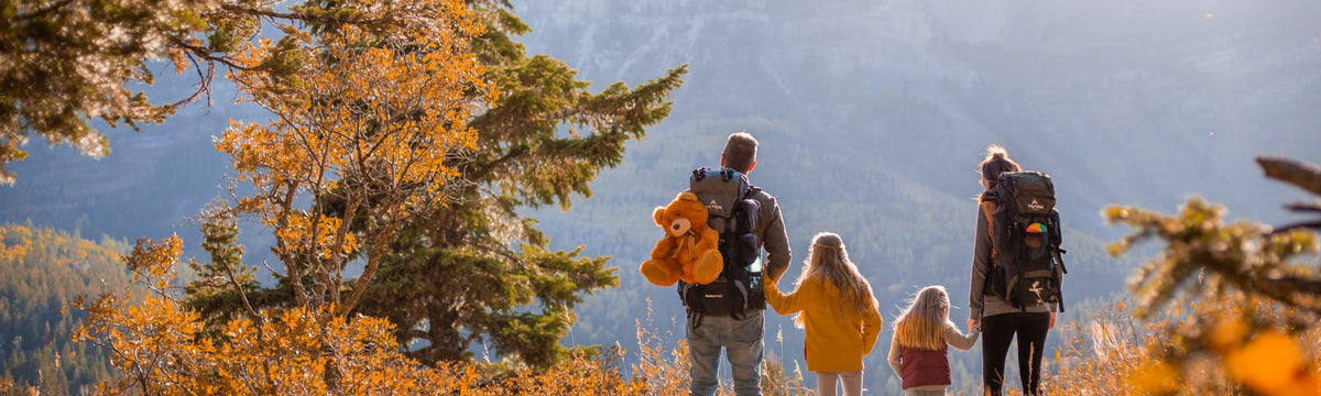 Father carrying a teddy bear on his backpacking pack while hiking with his family through autumn trees.