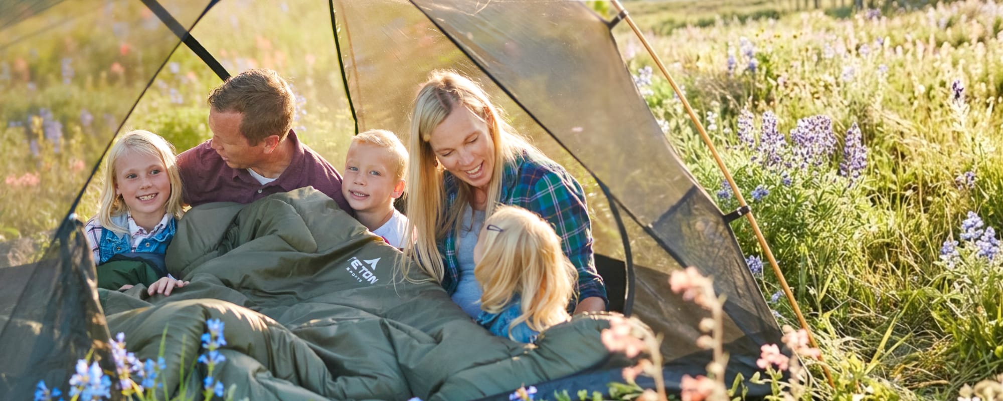 Family of five sitting inside a tent in a field with wildflowers