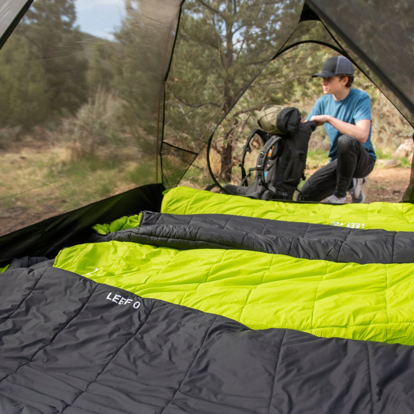 Person setting up camping gear inside a tent with a green and black mummy sleeping bag.