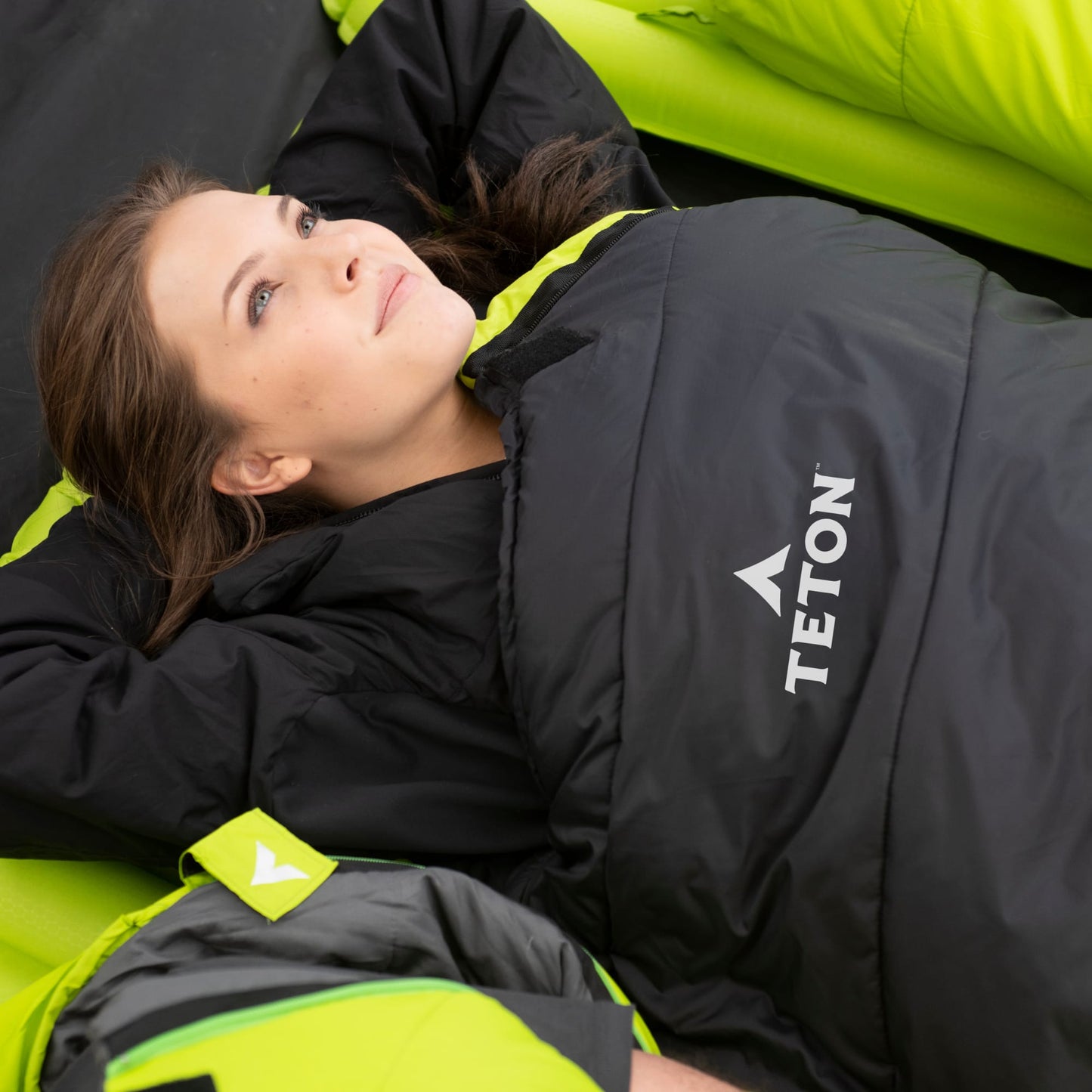 Person lying in a black and green sleeping bag with TETON logo
