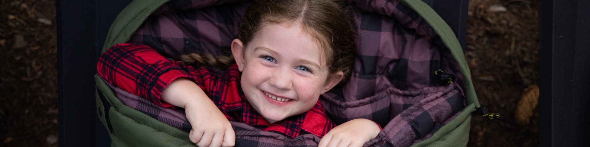 Child smiling and peeking out from inside the green bridger sleeping bag