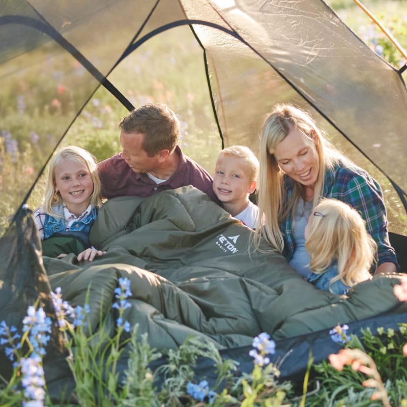 Family of five sitting inside a tent in a field with wildflowers