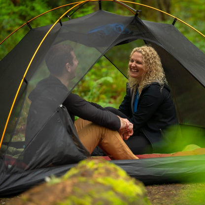 Two people laughing inside the mesh of Mountain Ultra 2-person tent in a forest setting without the cover.