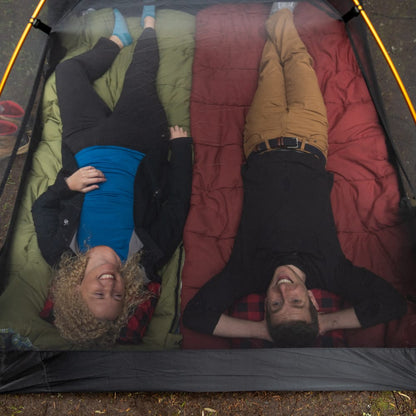 Two people laughing and lying inside the mesh of Mountain Ultra 2-person tent in a forest setting without the cover.