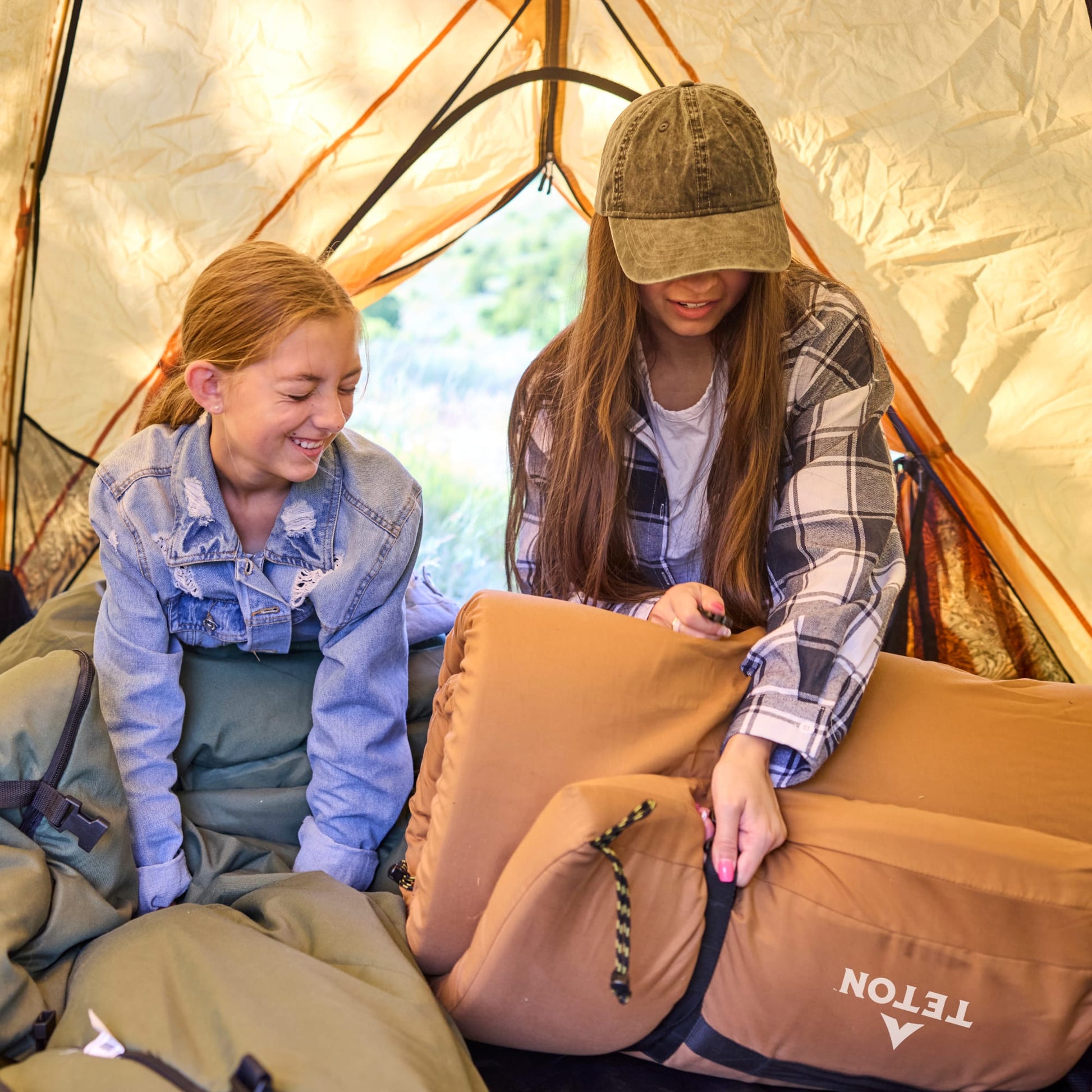 Two people inside a tent with a Teton brown canvas camping pad