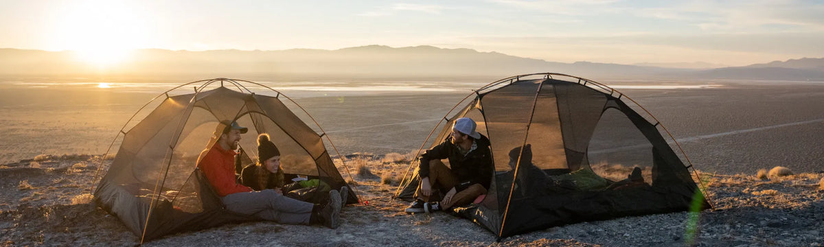 Friends relaxing in two Teton Mountain Ultra 2 person tent at golden hour, overlooking a desert valley.