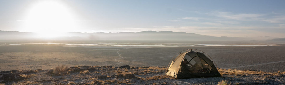 Solo backpacking tent pitched on a desert overlook with a hiker relaxing inside at sunset.
